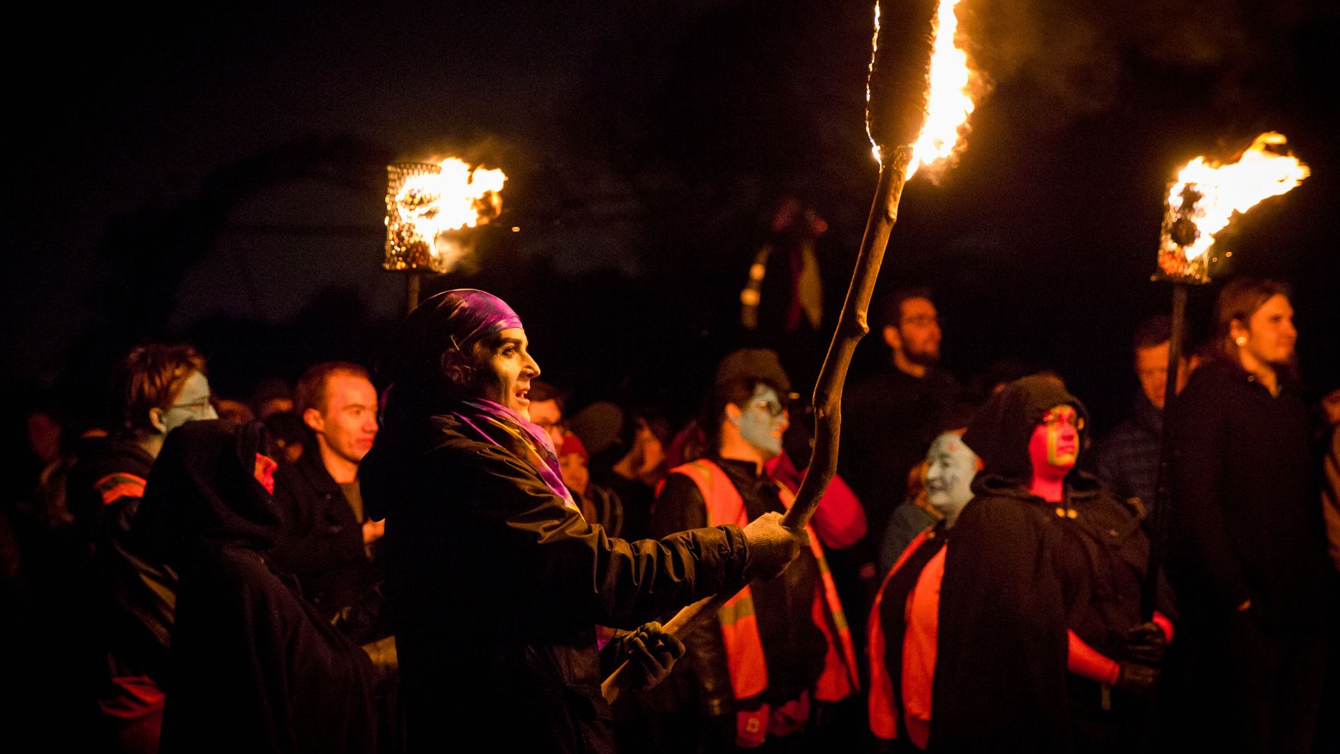 A group of people dressed in costumes and holding flaming torches while celebrating Halloween in Edinburgh.