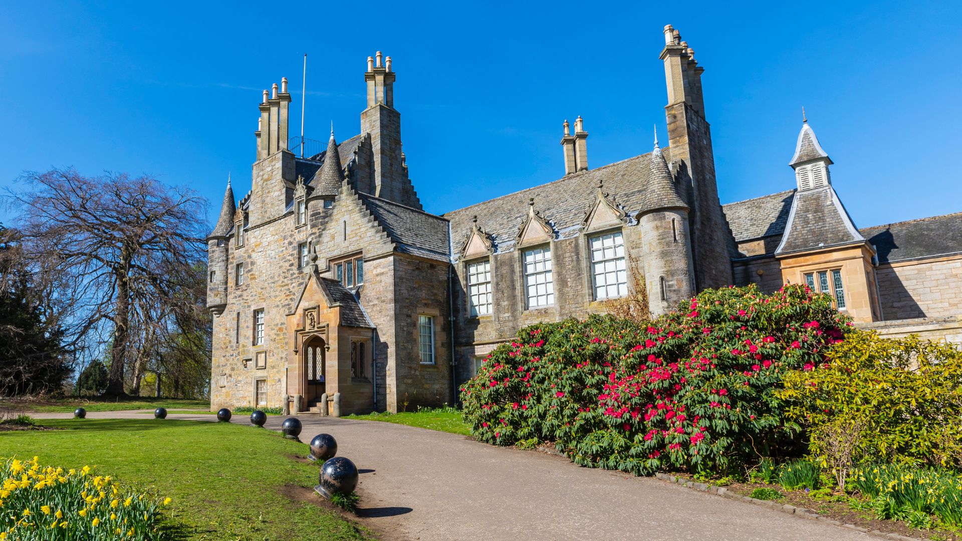 A small castle in Scotland with lots of chimneys and large flower bushes on a sunny day, host to Autumn crafting workshops.
