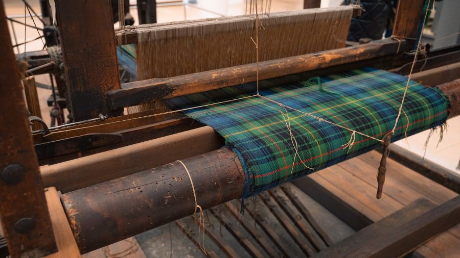 A section of green and blue tartan fabric on a wooden loom, on display at a museum in Edinburgh. 