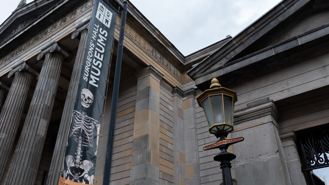 Neoclassical building with a gas light in one corner and a large banner reading Surgeons' Hall Museums, home to the remains of Burke and Hare.