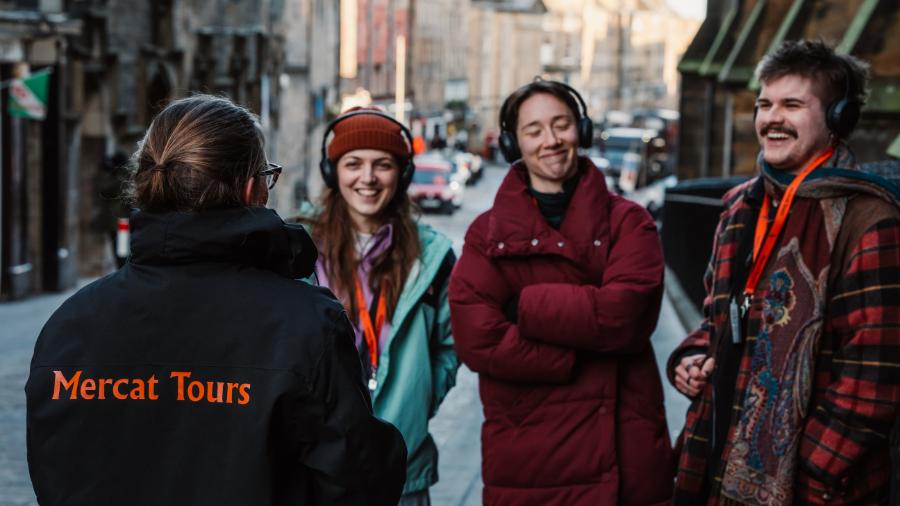 3 guests smiling and laughing at a Mercat Storyteller on the Royal Mile in Edinburgh during a history walking tour of Edinburgh.