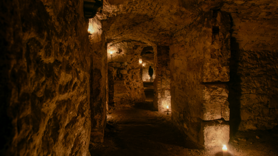 A corridor in the Edinburgh South Bridge Vaults leading into a room, the silhouette of a person standing at its far end.