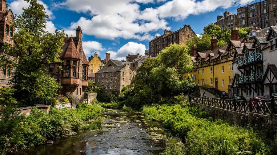 Dean Village in Edinburgh, with a small river running through it with old and colourful buildings on either side.