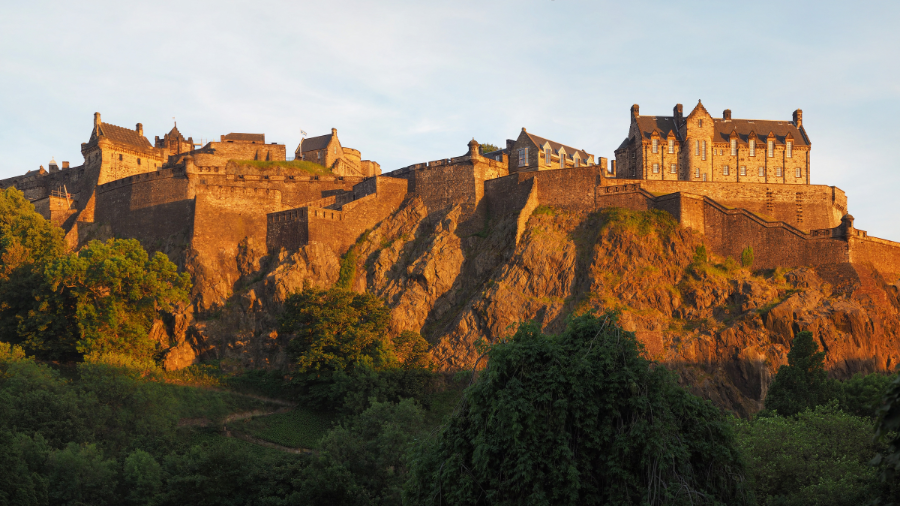 Edinburgh Castle perched atop craggy rocks, being lit by direct sunlight. 