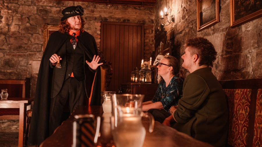 A Mercat Storyteller in a black cloak tells stories in the Megget’s Cellar of the Edinburgh Vaults.