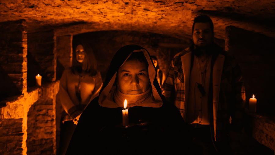 A Mercat Storyteller in a black cloak with the hood raised, in a corridor of the Edinburgh Vaults with a group of visitors behind her.