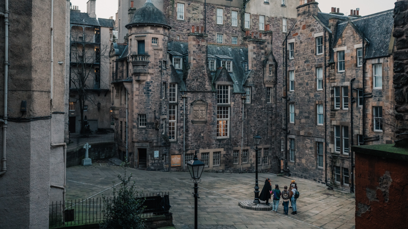 A Mercat Storyteller with a group of visitors on a ghost tour of Edinburgh in an empty courtyard next to the Writers' Museum. 