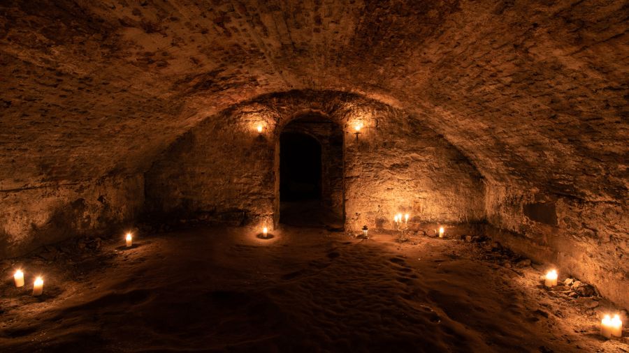 A candlelit stone room with an arched ceiling and open doorway, in the Blair Street Underground Vaults.