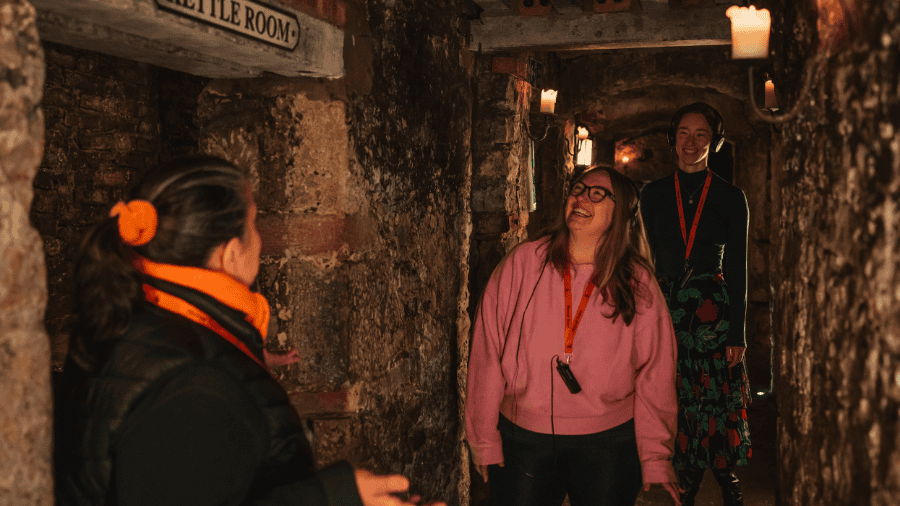 A Mercat Storyteller and two guests smiling during a tour of the Edinburgh underground vaults. 