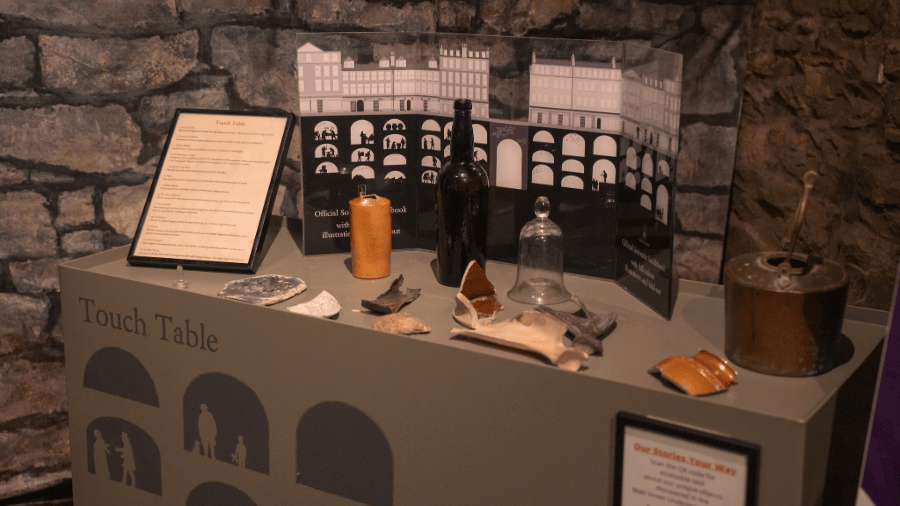 A table with various artefacts like bottles, pottery and bones, labelled ‘Touch Table’ in the Edinburgh Vaults Museum.