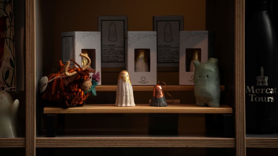A wool Highland cow ornament, two cement ghosts and a larger cement figure on a shelf in front of white Worrywart boxes.