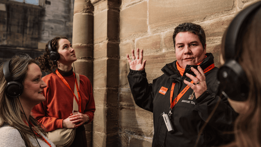 A Mercat Storyteller and three guests at the Mercat Cross at the beginning of an immersive Edinburgh history tour. 