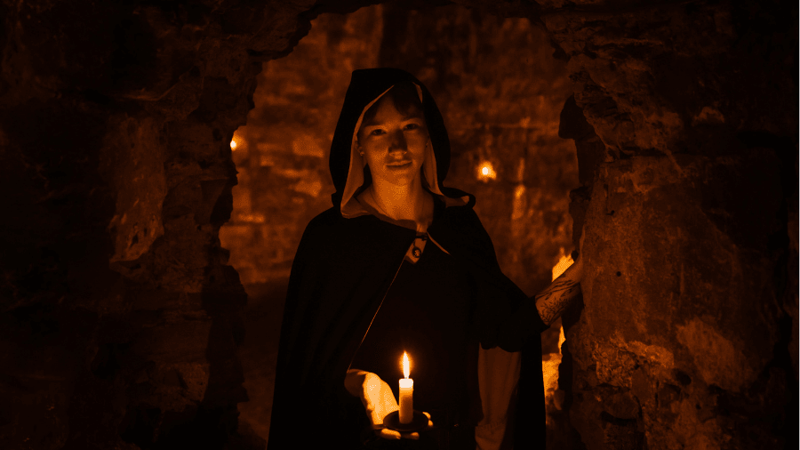 A Mercat Storyteller holding a lit candle and standing in an archway in the Edinburgh Blair Street Underground Vaults. 