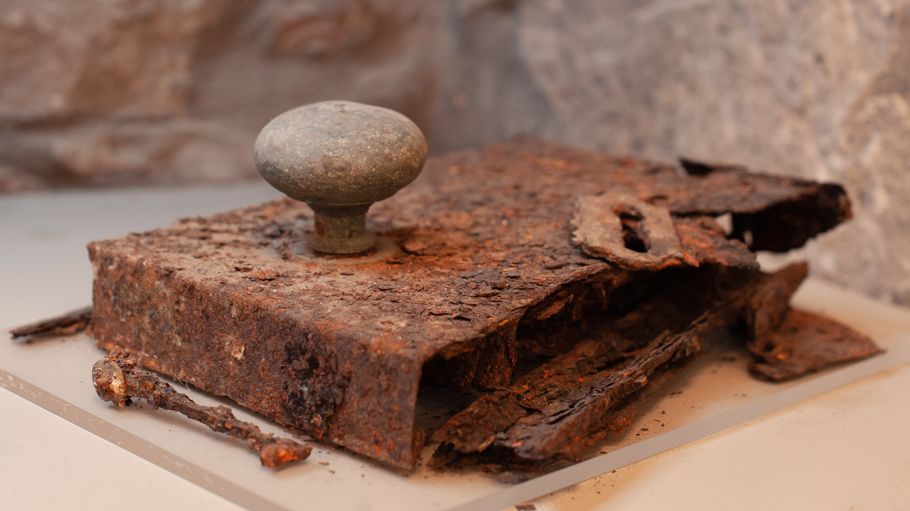 A large, very old and entirely rusted lock with the remains of a skeleton key next to it, on display in a museum case.