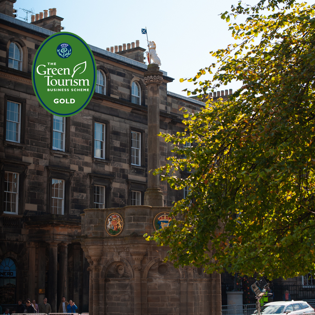 The Mercat Cross on Edinburgh's Royal Mile (a large, eight-sided monument), with a stone building behind. There is a tree in the foreground with green leaves and the 'Green Tourism Business Scheme GOLD Award logo' in the top right corner.