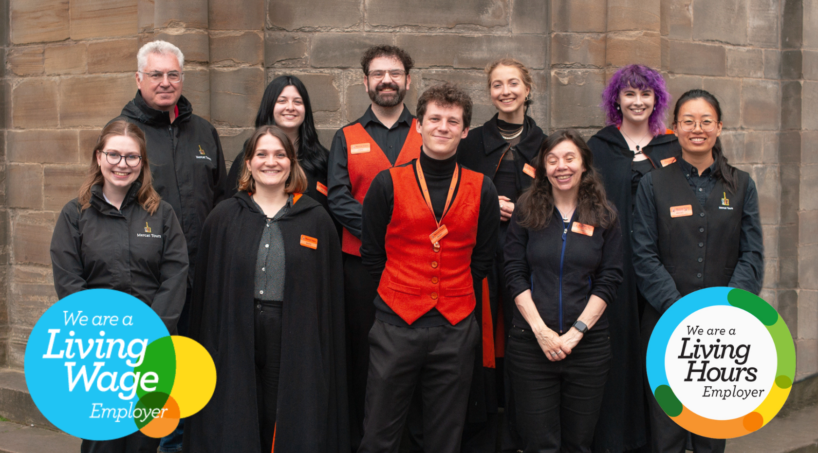 A group of 10 Mercat employees standing in front of the Edinburgh Mercat Cross, smiling. A Living Wage Employer graphic is in the bottom left corner, a Living Hours Employer graphic in the bottom right.