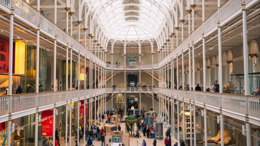 The main hall of the National Museum of Scotland: three levels of balconies looking onto a hall filled with interactive displays.
