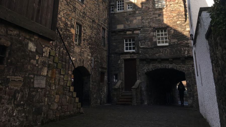 A person walking through a stone archway into a Royal Mile close.