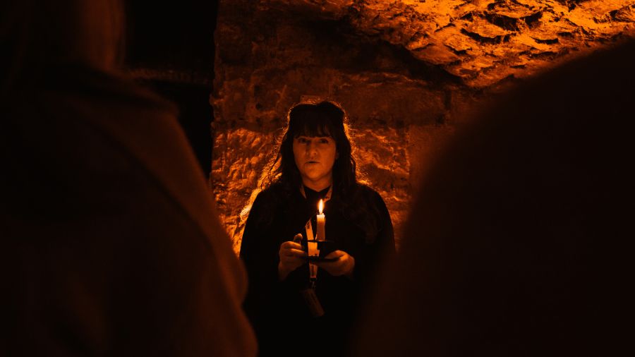 A Mercat Storyteller holding a lit candle in the Edinburgh Vaults on an Edinburgh ghost tour. https://www.mercatto