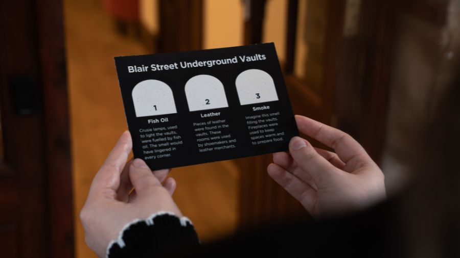 A photo taken over a woman’s shoulder as she looks at a scratch-and-sniff card featuring three scents from the Edinburgh Vaults: fish oil, leather and smoke.
