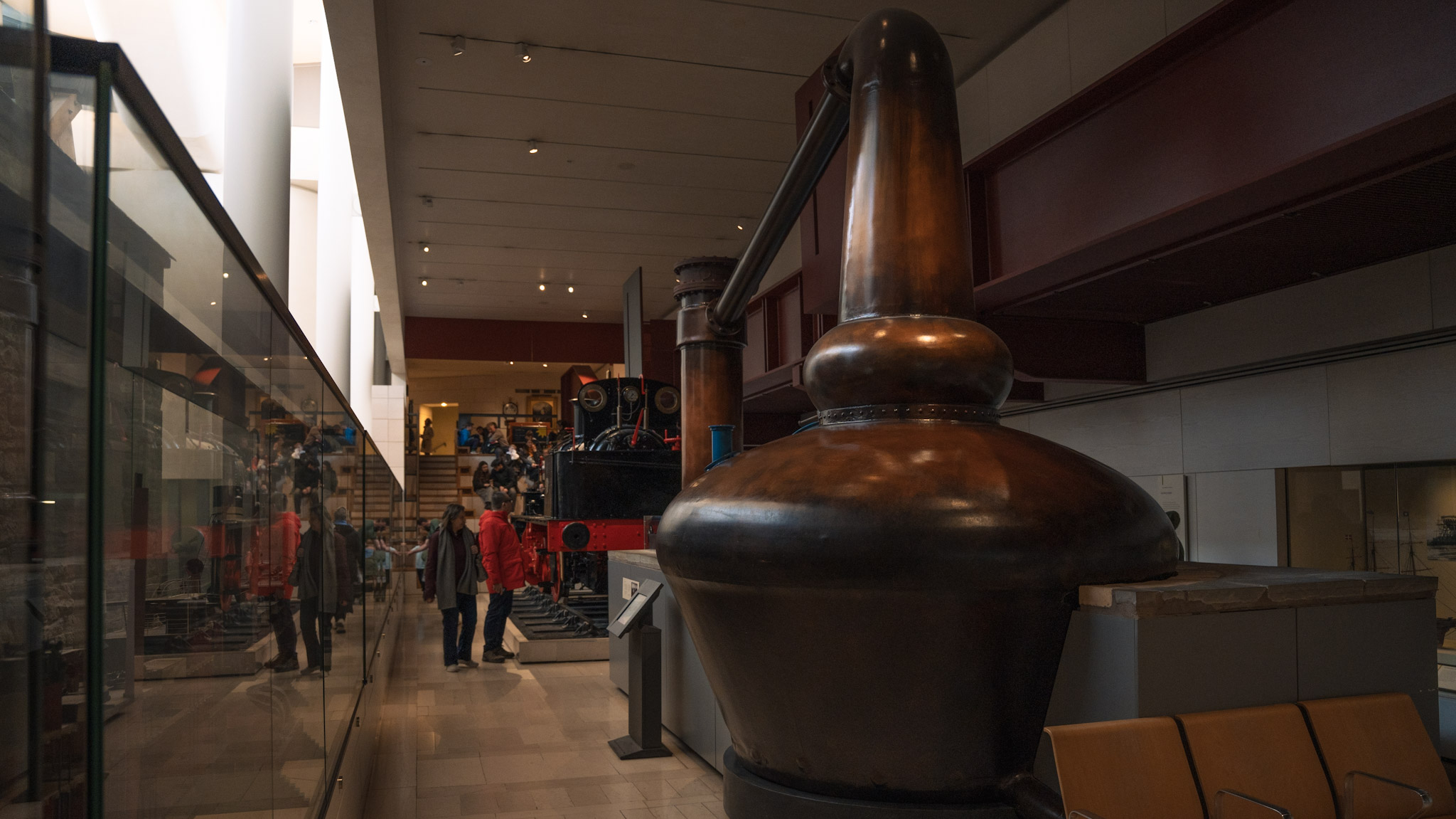 A very large copper whisky still on display in a museum, next to a small train engine display. 