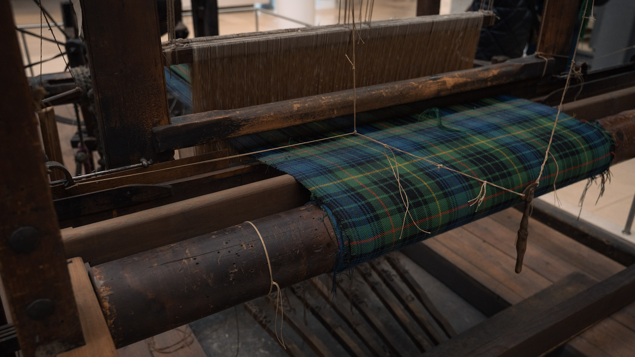 A section of green and blue tartan fabric on a wooden loom, on display at a museum in Edinburgh. 