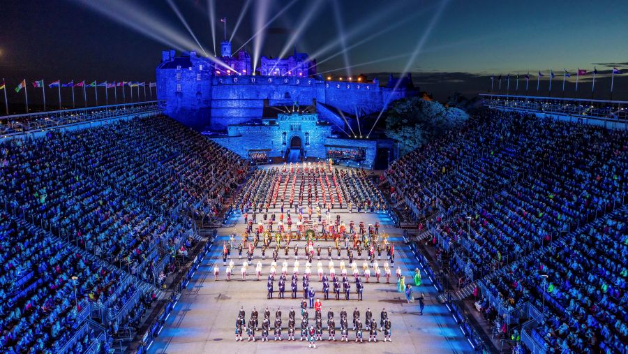The Edinburgh Tattoo, featuring marching musicians between two large audience stands and with Edinburgh Castle lit up at the end.