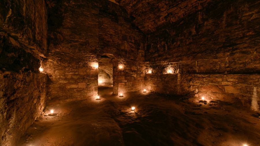  A tall room in the Edinburgh vaults, lit by candles and featuring arching doorways and ceilings.