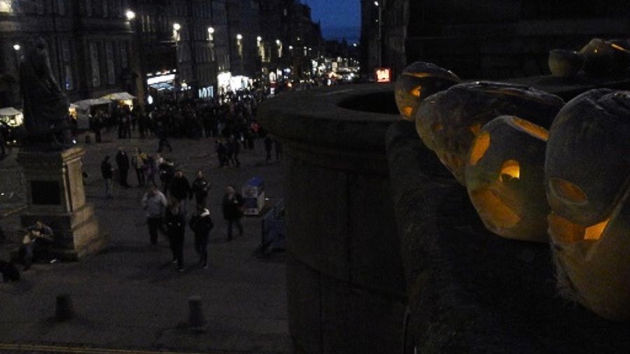 A series of carved turnips, glowing from the inside, lined up on the edge of the Edinburgh Mercat Cross on Halloween.