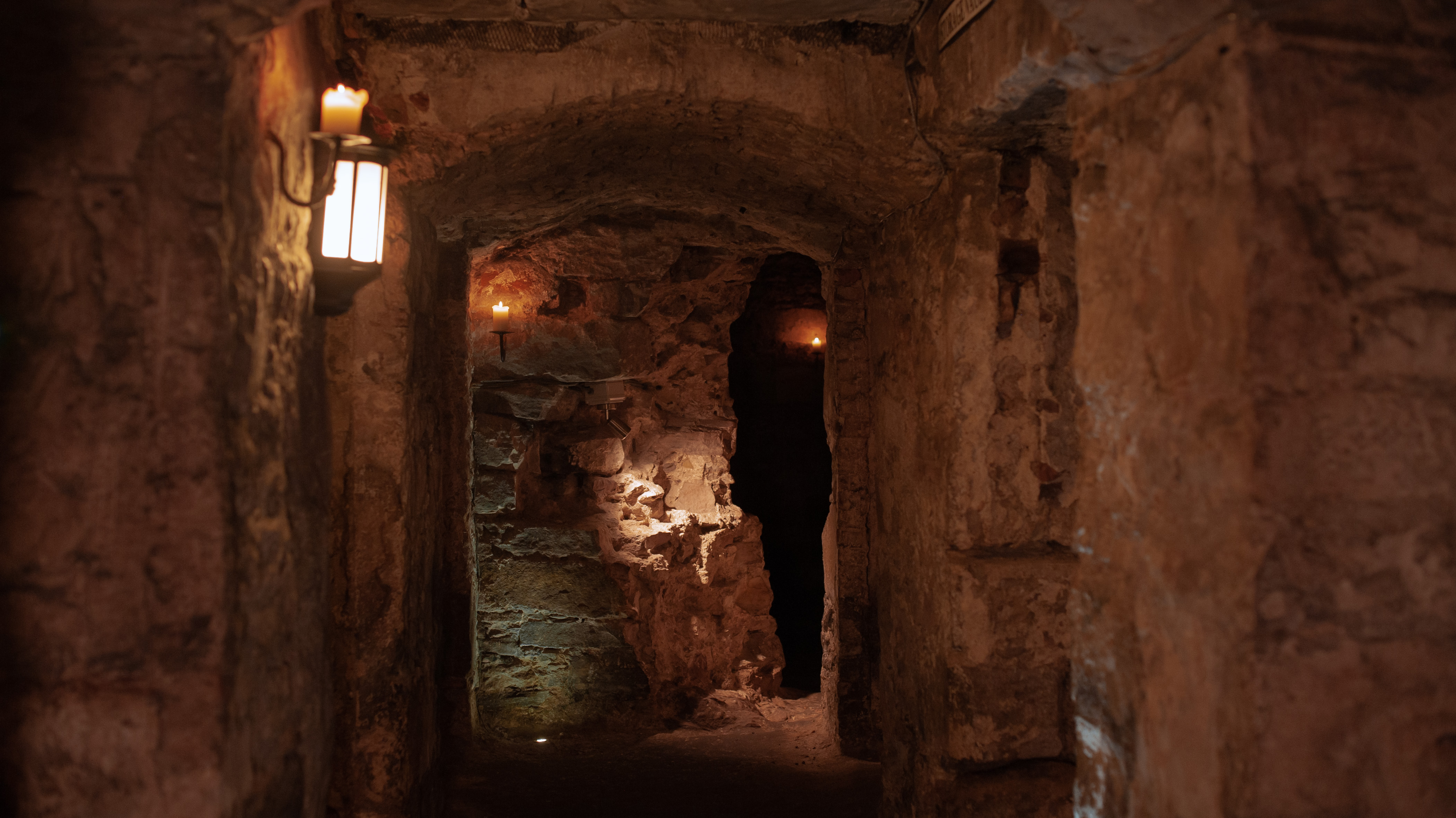 A corridor in the Blair Street Underground Vaults, lit mostly by candles and with archways leading off in all directions.