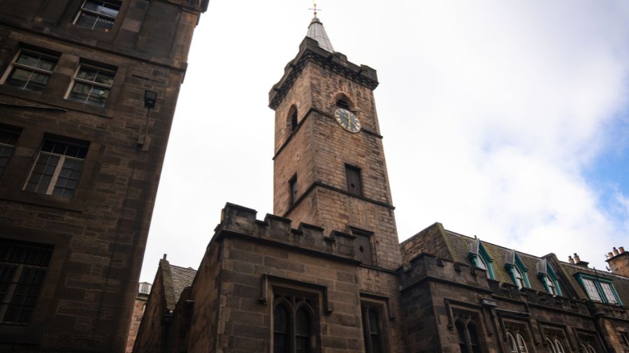 An old stone building with a tall, rectangular tower with a clock, and crenellations along its rooflines.