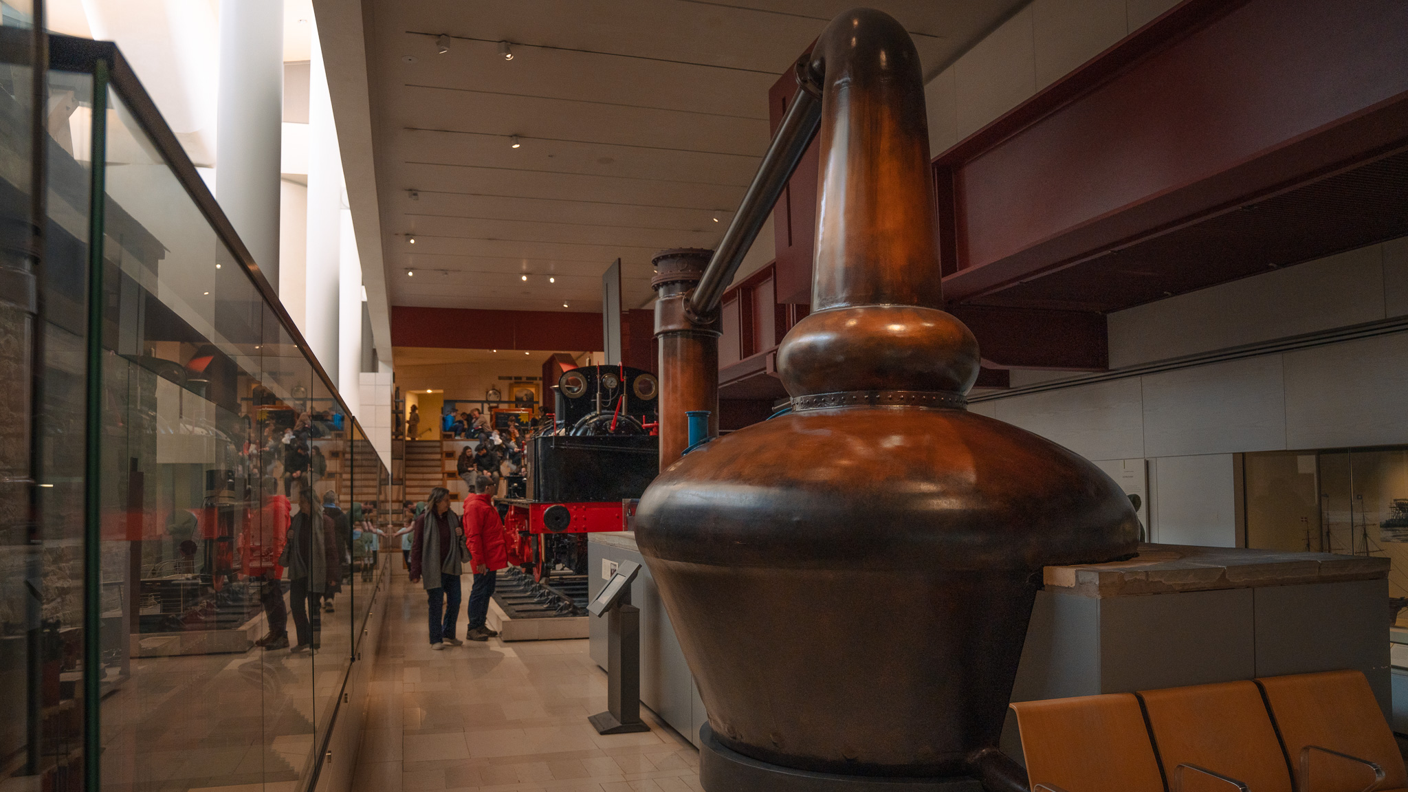 A very large copper whisky still on display in a museum, next to a small train engine display. 