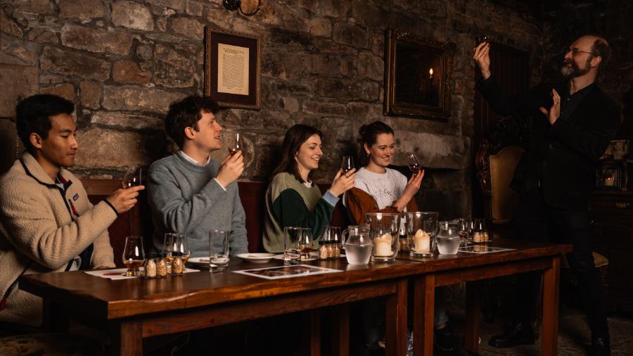 A Mercat Storyteller leading 4 people in a whisky tasting in a candlelit room of the Edinburgh vaults.