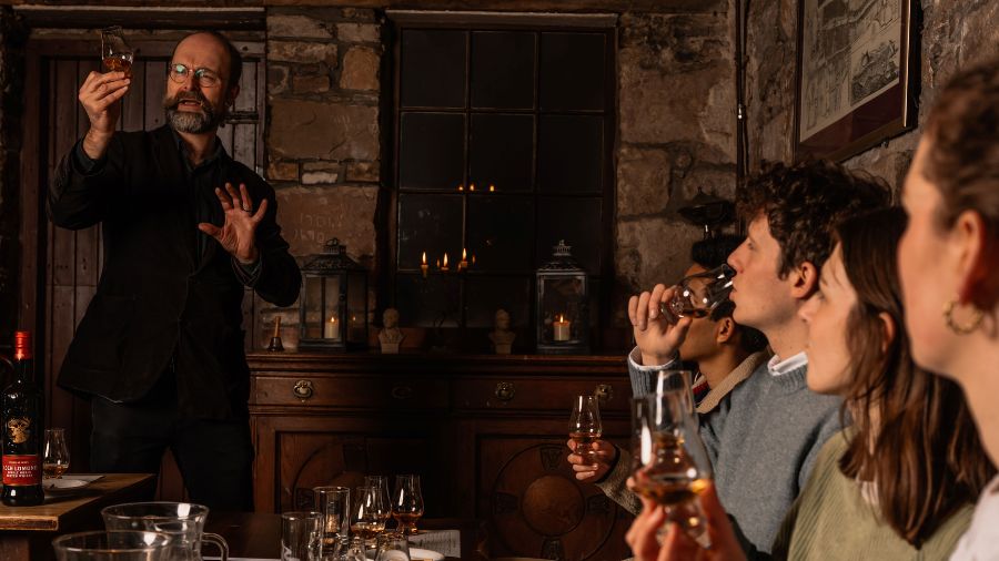 A group of people watching a Master Mercat Storyteller make a toast during an Edinburgh Whisky Tour & Tasting for Burns Night.