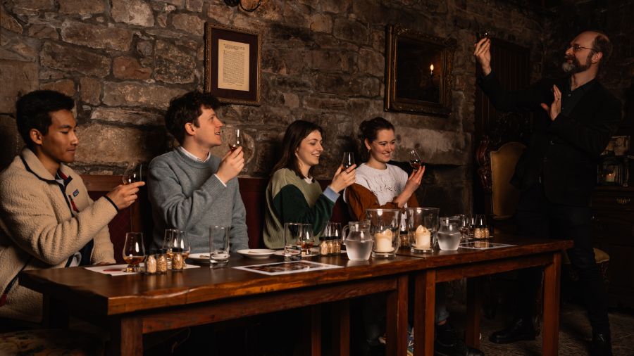 Four people in the candlelit Megget’s Cellar, being led through a Scotch whisky tasting by a Mercat Storyteller