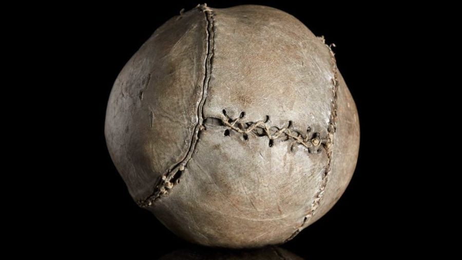 An image from The Stirling Smith Art Gallery & Museum of a dried-out leather ball against a black background, the ball showing stitched seams.