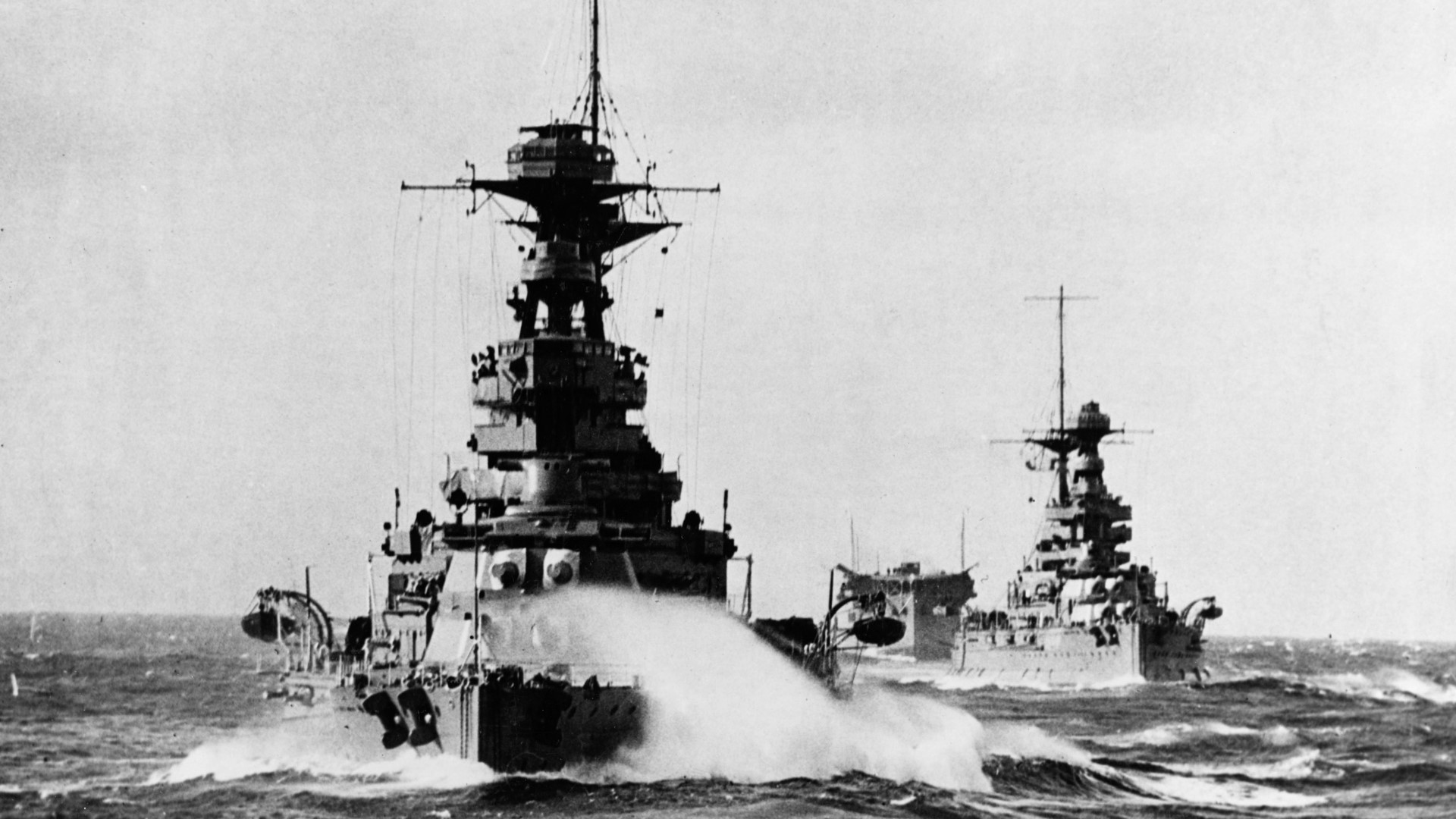 A World War II military ship moving across a body of water, another ship behind it. 